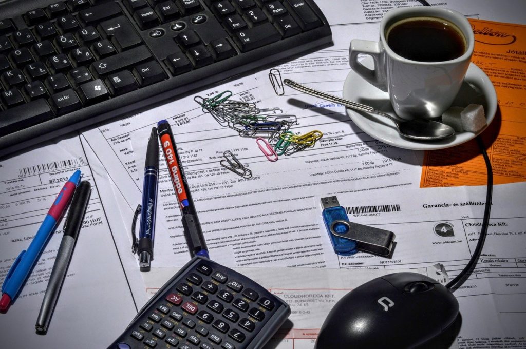 A keyboard, computer mouse, pendrive, pens, documents and coffee cup on a desk