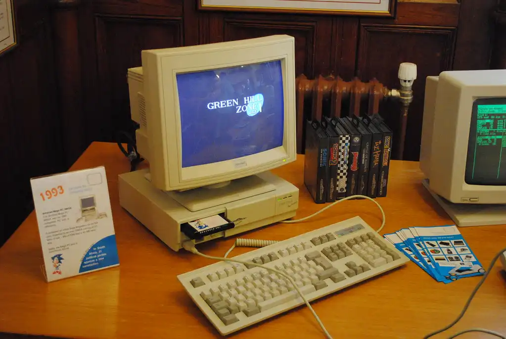 An old computer with a keyboard and a cartridge on a desk