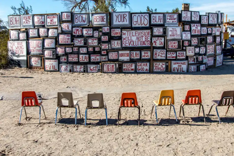 A picture showing a wall built from TVs "displaying" various statements with a row of chairs before it