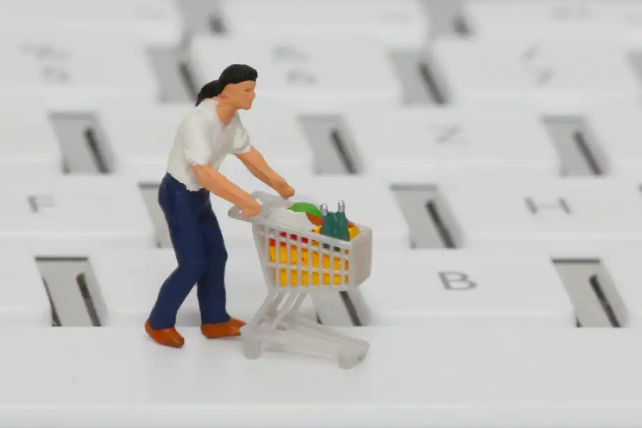 A plastic figure is standing on a keyboard. A figure is a man that has a shopping cart full of groceries