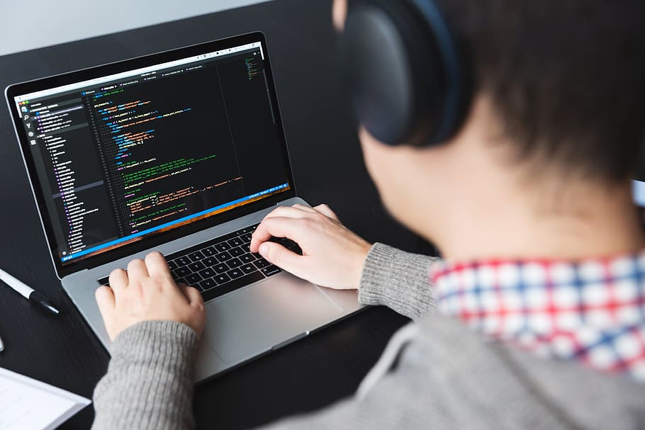 mężczyzna w słuchawkach piszący kod na macbooku