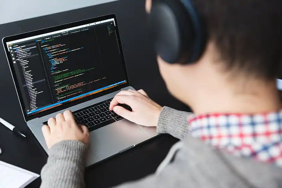 mężczyzna w słuchawkach piszący kod na macbooku